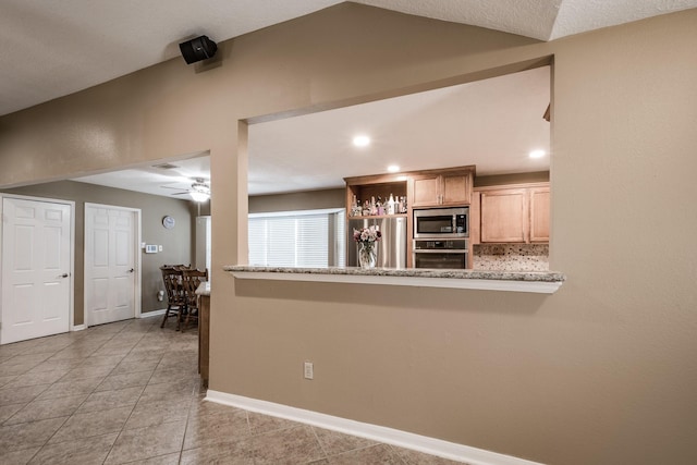 kitchen featuring kitchen peninsula, light stone counters, light brown cabinets, and appliances with stainless steel finishes