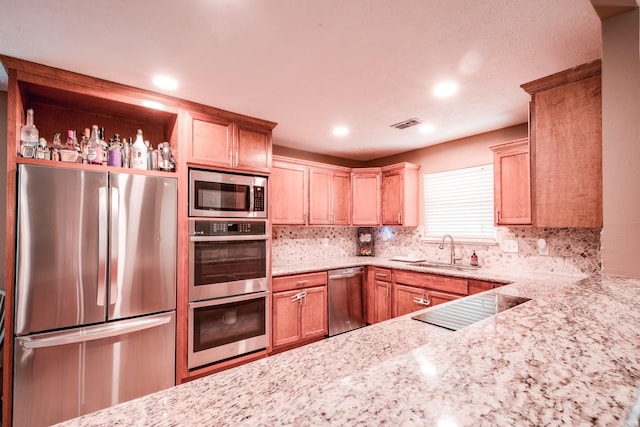 kitchen featuring backsplash, light stone counters, sink, and appliances with stainless steel finishes