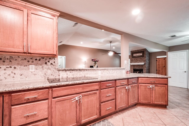 kitchen featuring black electric stovetop, vaulted ceiling, light stone countertops, a fireplace, and tasteful backsplash