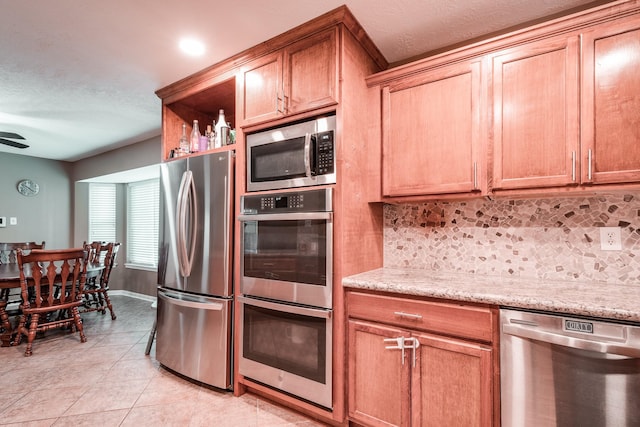 kitchen with stainless steel appliances, light stone counters, tasteful backsplash, and light tile patterned flooring