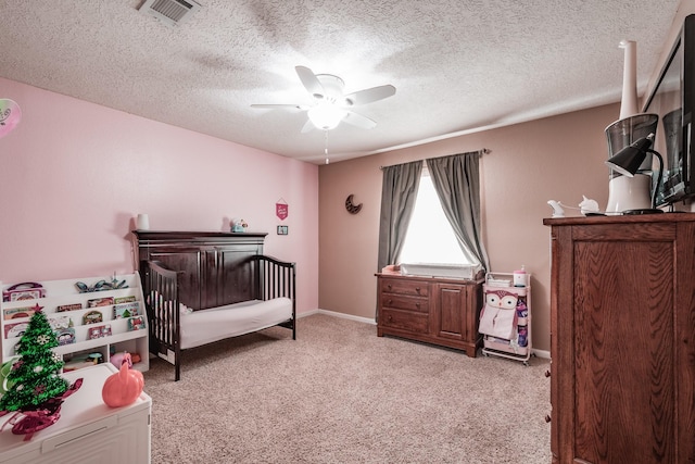 bedroom with a crib, a textured ceiling, light colored carpet, and ceiling fan