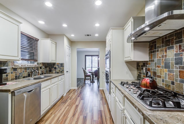 kitchen featuring wall chimney range hood, sink, light hardwood / wood-style flooring, tasteful backsplash, and stainless steel appliances