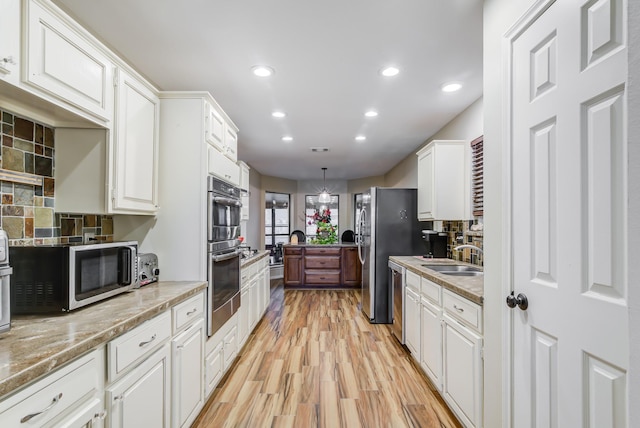 kitchen featuring decorative backsplash, white cabinets, pendant lighting, and appliances with stainless steel finishes