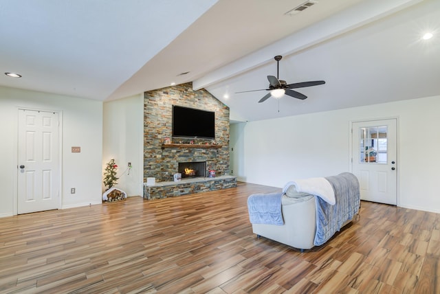 living room with wood-type flooring, vaulted ceiling with beams, a stone fireplace, and ceiling fan