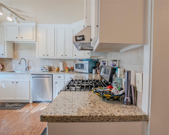 kitchen with stainless steel appliances, hardwood / wood-style flooring, white cabinets, backsplash, and sink