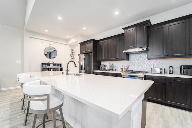 kitchen with decorative backsplash, appliances with stainless steel finishes, sink, a center island with sink, and a breakfast bar area