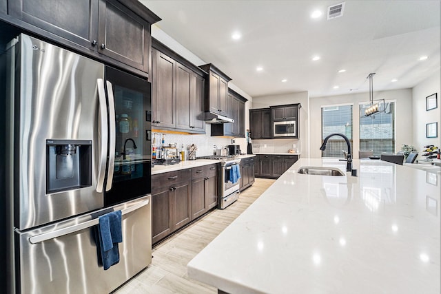 kitchen with appliances with stainless steel finishes, light stone counters, sink, pendant lighting, and light hardwood / wood-style flooring