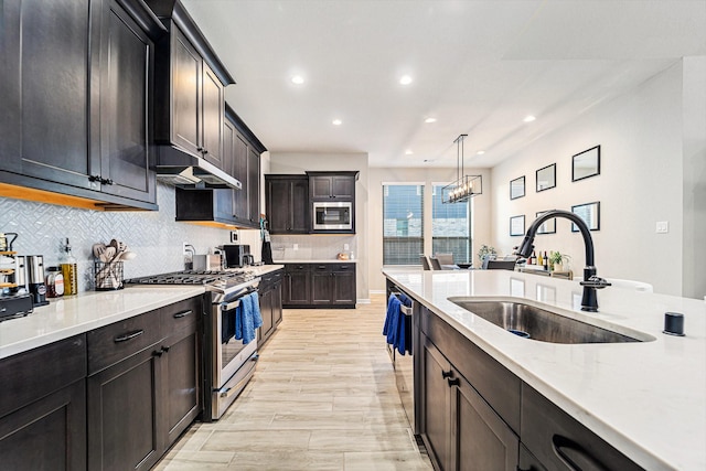 kitchen with pendant lighting, sink, appliances with stainless steel finishes, tasteful backsplash, and light hardwood / wood-style floors