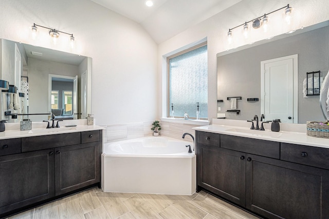 bathroom featuring vanity, a tub, a wealth of natural light, and vaulted ceiling