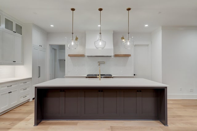 kitchen featuring backsplash, white cabinets, light hardwood / wood-style flooring, and an island with sink