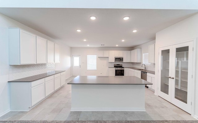 kitchen with sink, appliances with stainless steel finishes, white cabinetry, a kitchen island, and french doors