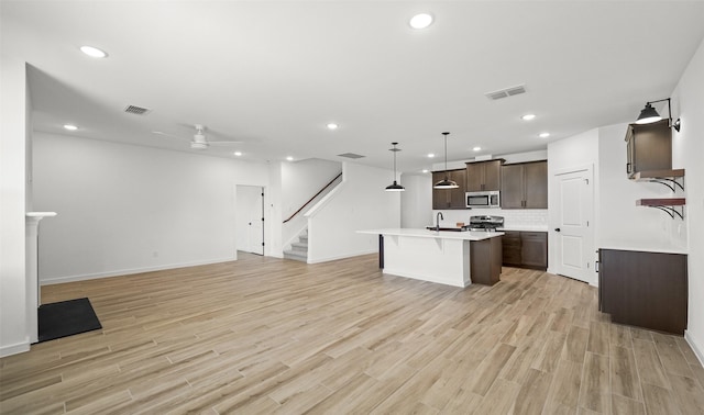 kitchen featuring a center island with sink, sink, hanging light fixtures, stainless steel appliances, and dark brown cabinets