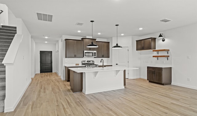 kitchen featuring pendant lighting, decorative backsplash, dark brown cabinetry, light wood-type flooring, and stainless steel appliances