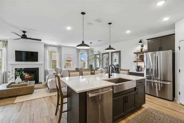 kitchen with hanging light fixtures, light wood-type flooring, appliances with stainless steel finishes, and a center island with sink