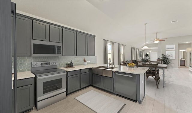 kitchen with kitchen peninsula, decorative backsplash, stainless steel appliances, vaulted ceiling, and sink