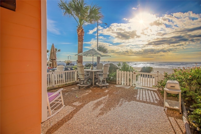 patio terrace at dusk with a grill, a water view, and a beach view