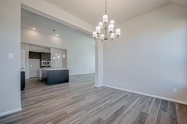 interior space with hardwood / wood-style floors, stainless steel microwave, a center island with sink, decorative light fixtures, and a notable chandelier