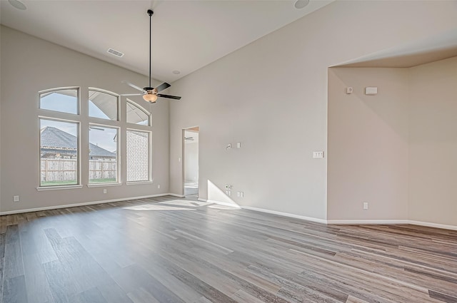 unfurnished living room featuring ceiling fan, light wood-type flooring, and a high ceiling