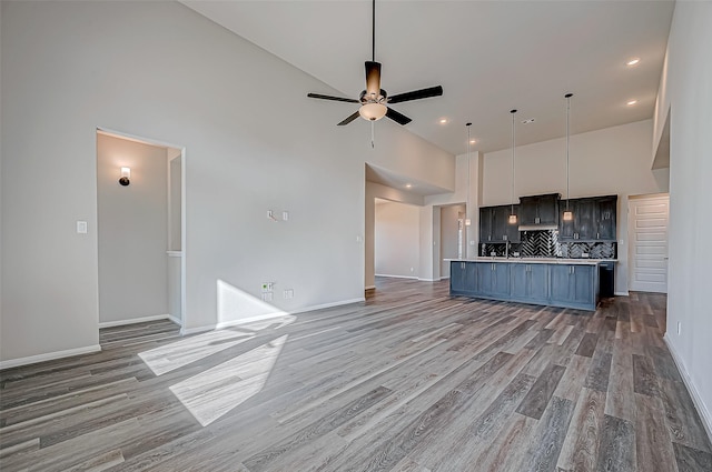 kitchen with high vaulted ceiling, hanging light fixtures, ceiling fan, decorative backsplash, and light hardwood / wood-style floors