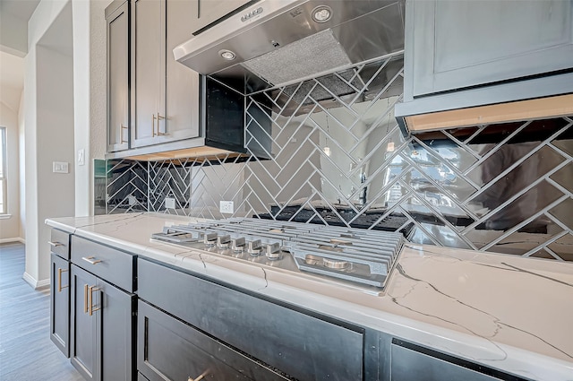 kitchen with tasteful backsplash, light stone counters, gray cabinetry, light hardwood / wood-style floors, and range hood