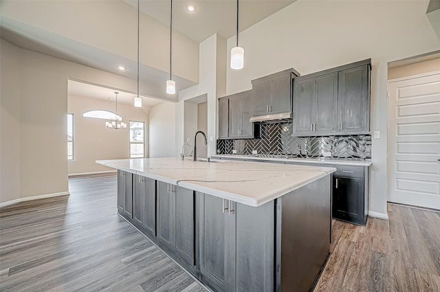 kitchen featuring light stone countertops, sink, pendant lighting, a kitchen island with sink, and light wood-type flooring