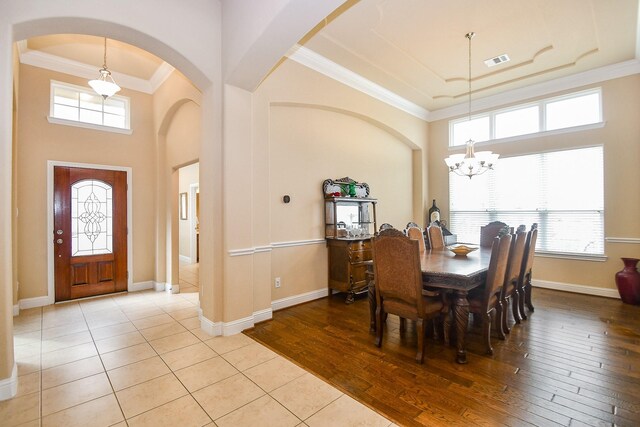 dining space featuring a high ceiling, ornamental molding, a notable chandelier, and light wood-type flooring