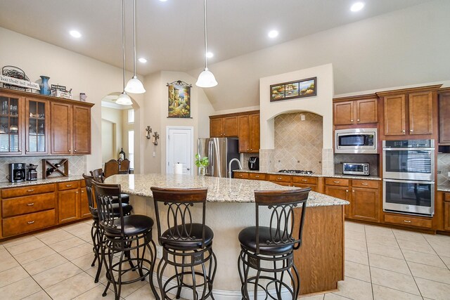 kitchen with a center island with sink, hanging light fixtures, tasteful backsplash, a breakfast bar area, and stainless steel appliances