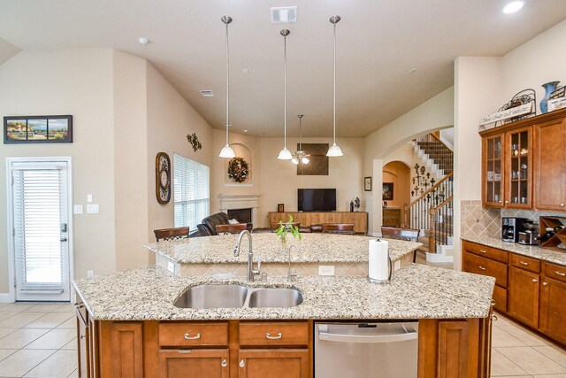 kitchen with stainless steel dishwasher, light tile patterned floors, sink, and a kitchen island with sink