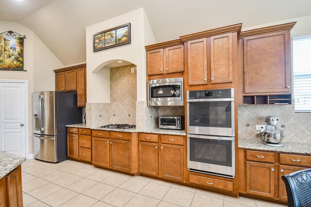 kitchen featuring decorative backsplash, light stone counters, lofted ceiling, and stainless steel appliances