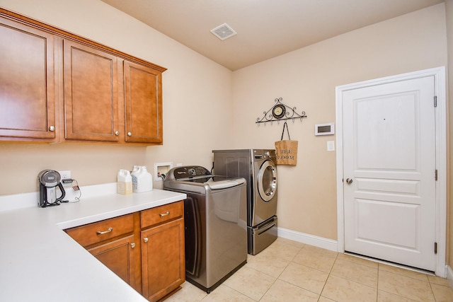 clothes washing area with cabinets, light tile patterned floors, and washing machine and clothes dryer