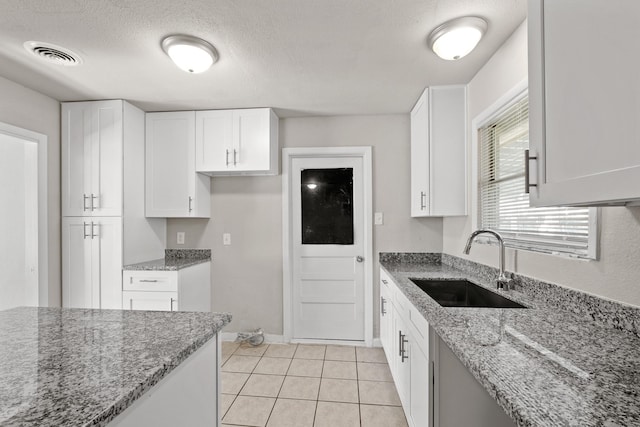 kitchen featuring stone counters, white cabinets, sink, light tile patterned floors, and a textured ceiling