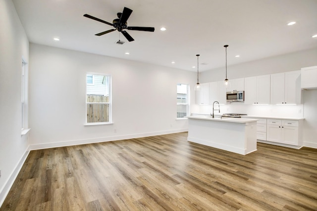 kitchen featuring white cabinets, decorative light fixtures, a kitchen island with sink, and light hardwood / wood-style flooring