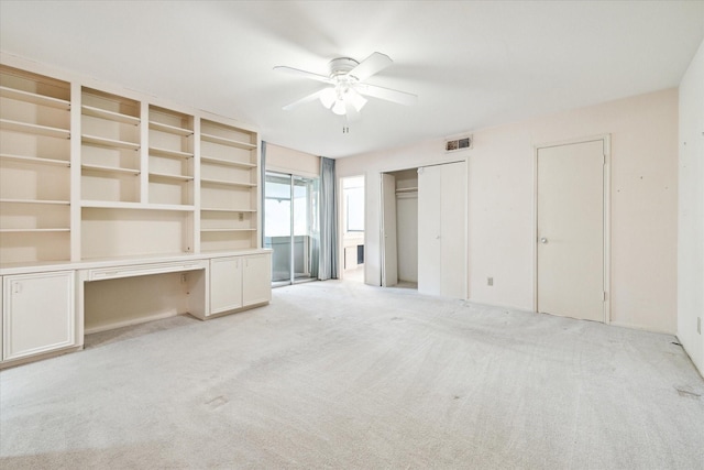 unfurnished bedroom with ceiling fan, light colored carpet, and built in desk