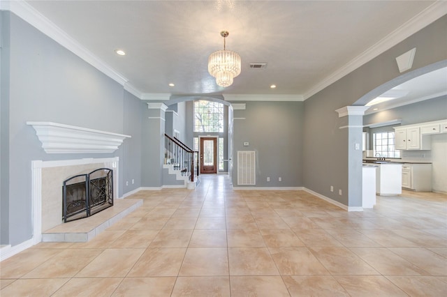 unfurnished living room with a chandelier, crown molding, a wealth of natural light, and a tiled fireplace