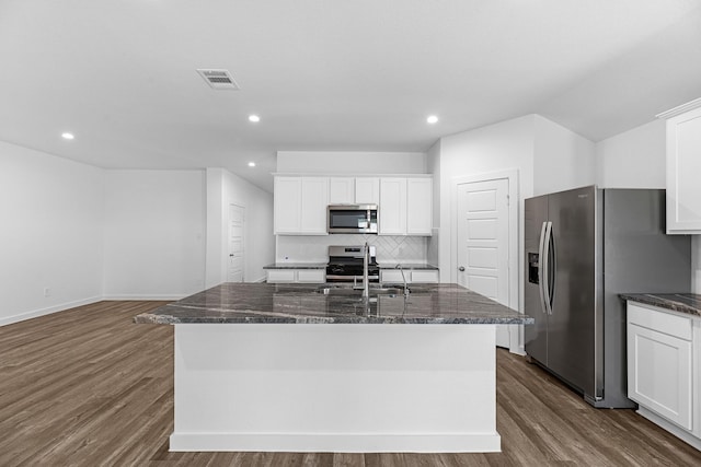 kitchen featuring white cabinetry, tasteful backsplash, dark stone countertops, a kitchen island with sink, and appliances with stainless steel finishes