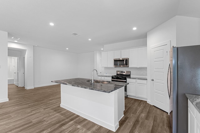 kitchen with white cabinetry, sink, stainless steel appliances, dark stone countertops, and a kitchen island with sink