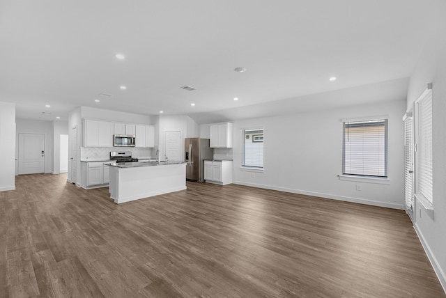 kitchen with hardwood / wood-style floors, backsplash, an island with sink, appliances with stainless steel finishes, and white cabinetry