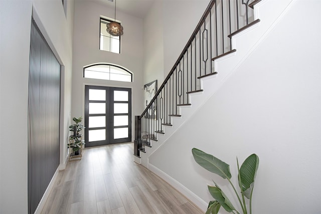 foyer entrance featuring light wood-type flooring, a towering ceiling, and french doors