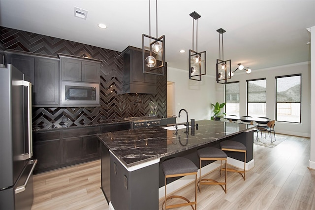 kitchen featuring pendant lighting, dark stone counters, a center island with sink, sink, and appliances with stainless steel finishes