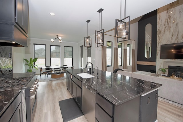 kitchen with appliances with stainless steel finishes, a spacious island, dark stone countertops, light hardwood / wood-style floors, and hanging light fixtures