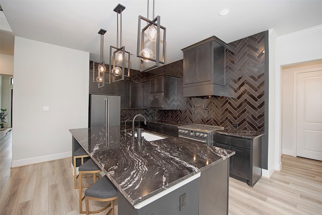 kitchen featuring high quality appliances, sink, hanging light fixtures, an island with sink, and tasteful backsplash