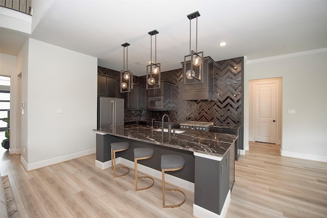 kitchen featuring built in microwave, hanging light fixtures, high end refrigerator, dark stone counters, and a kitchen bar