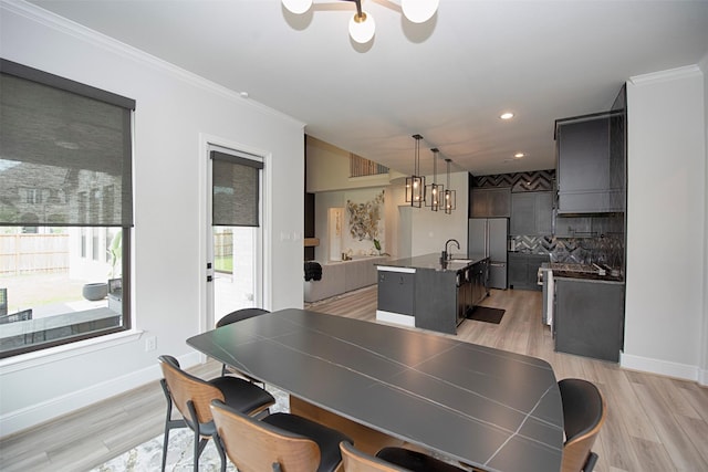 dining area featuring sink, an inviting chandelier, ornamental molding, and light hardwood / wood-style flooring