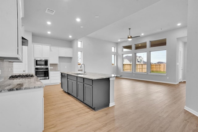 kitchen featuring light stone countertops, white cabinetry, ceiling fan, a kitchen island with sink, and decorative backsplash