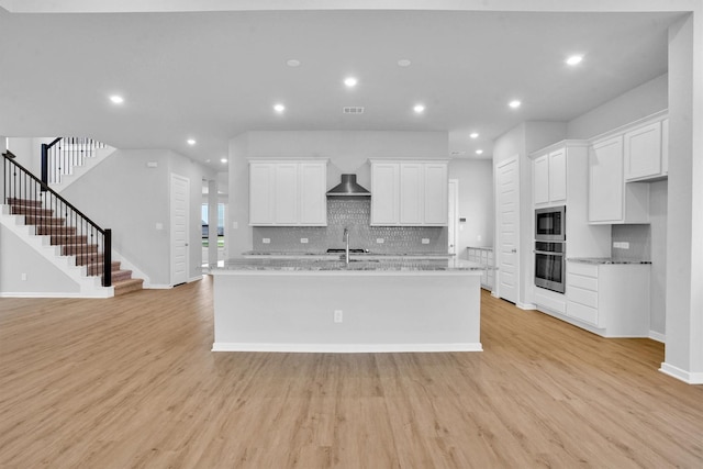 kitchen featuring light wood-type flooring, light stone counters, white cabinetry, and stainless steel oven