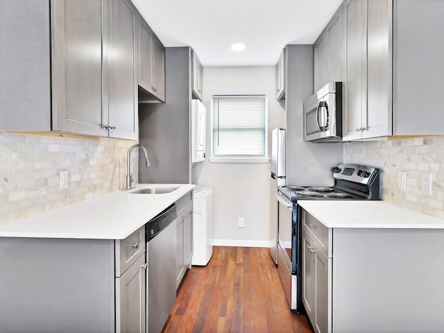 kitchen with sink, dark wood-type flooring, stainless steel appliances, gray cabinets, and decorative backsplash