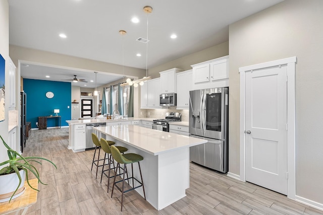 kitchen featuring stainless steel appliances, a kitchen island, ceiling fan, and white cabinetry