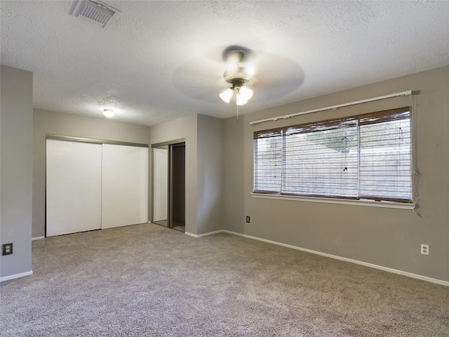 unfurnished bedroom with two closets, ceiling fan, light colored carpet, and a textured ceiling