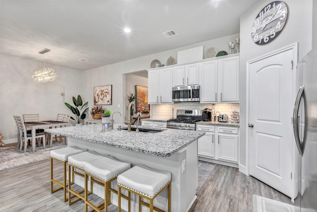 kitchen featuring a kitchen island with sink, white cabinets, decorative light fixtures, light hardwood / wood-style floors, and stainless steel appliances