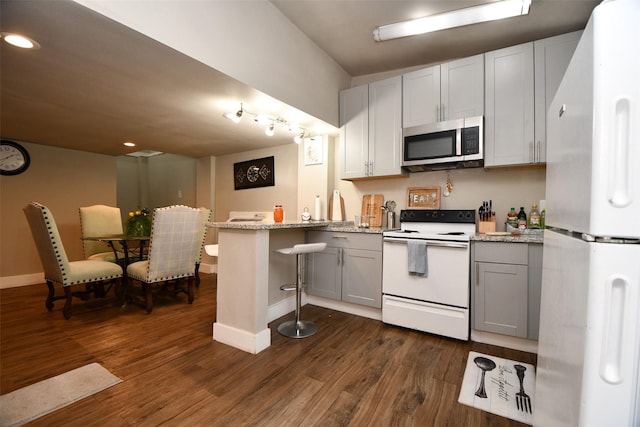 kitchen with light stone counters, white appliances, dark hardwood / wood-style flooring, and white cabinets